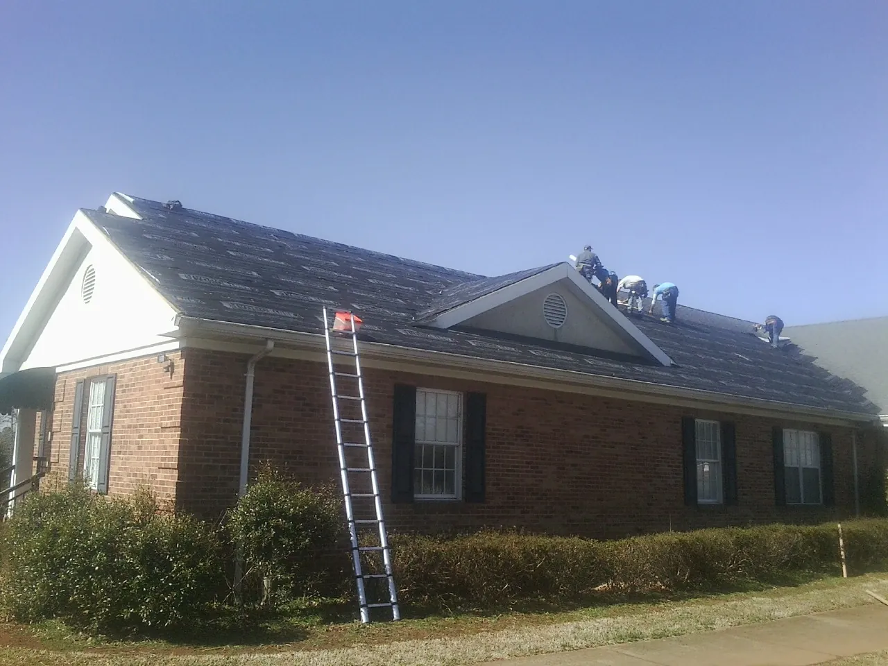 Crew tearing shingles off a brick ranch roof with a ladder set — Emergency Roof Repair work by our crew in Adams
