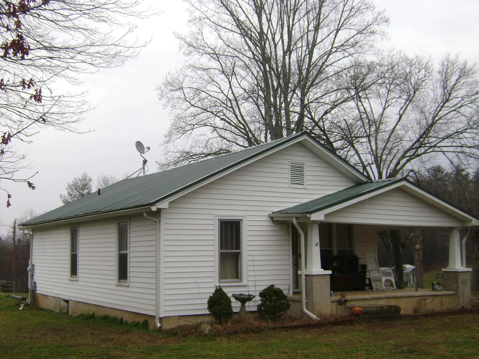 Green metal roof on a white bungalow with a side porch in Adams